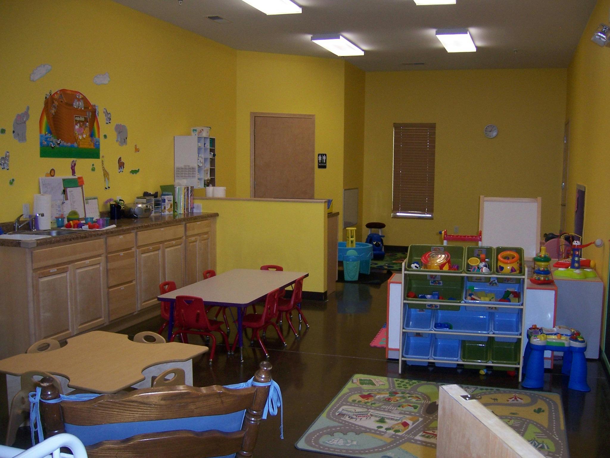 Empty classroom with yellow walls, tables, and toy storage