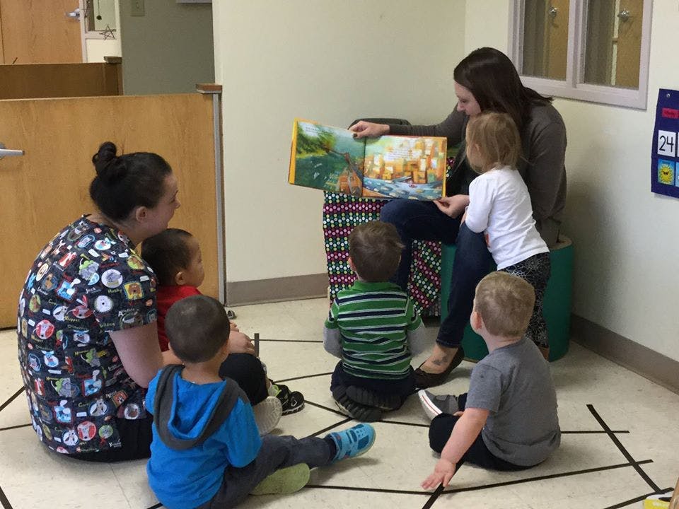 Two people reading a book to multiple children in a classroom