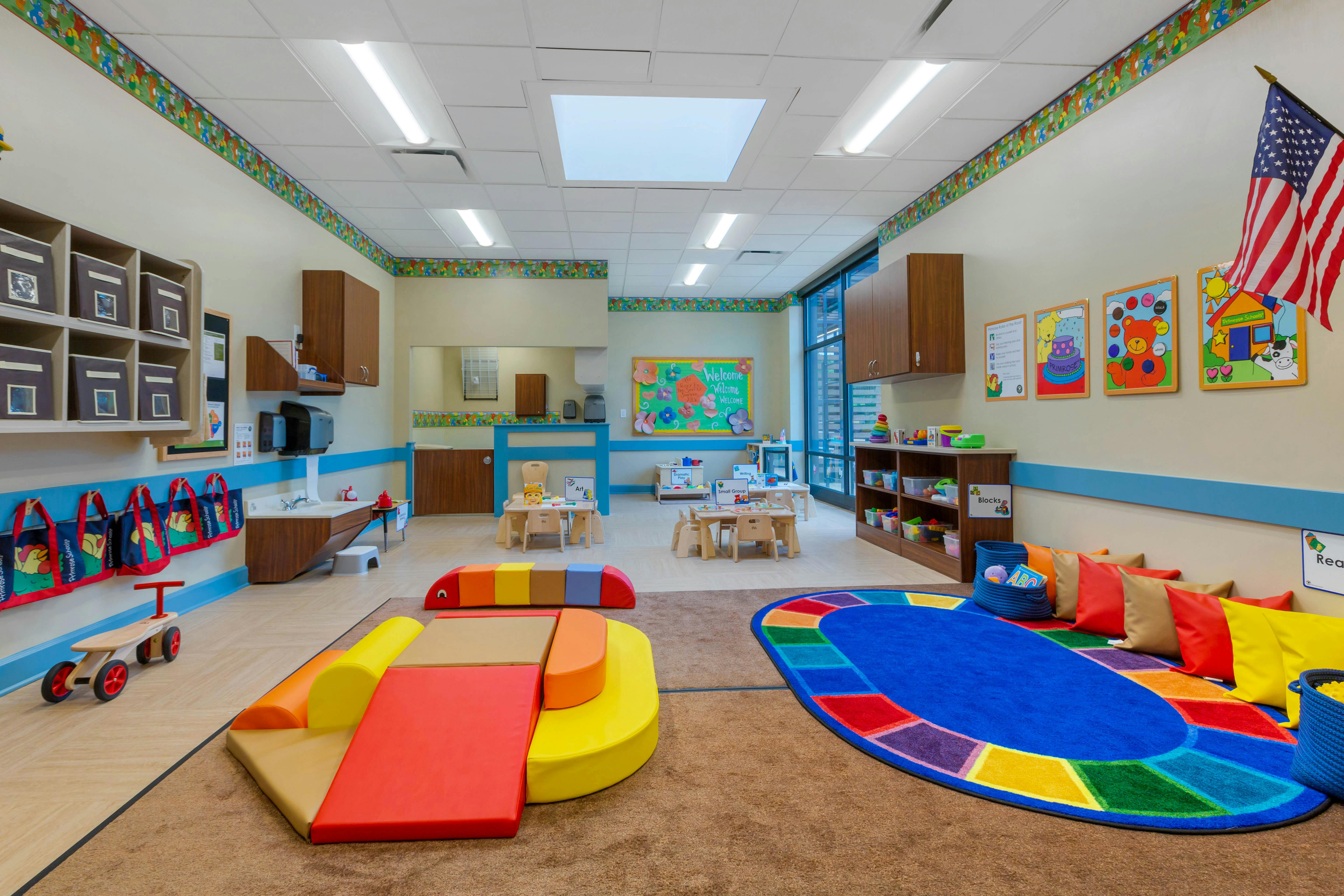 Classroom with small tables and chairs, colorful play mats, and an American flag