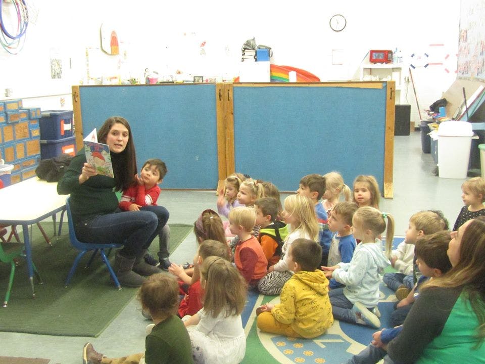 Person reading a book to a group of children in a classroom