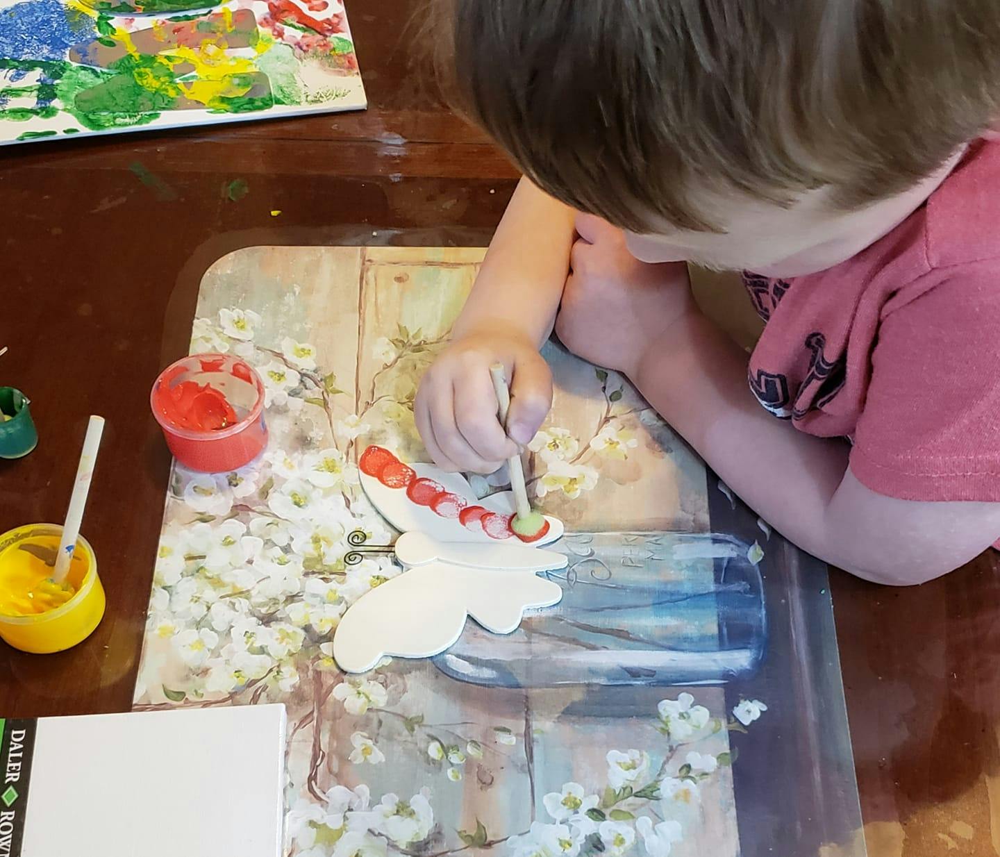 Child painting a white cutout shape with red and green paint