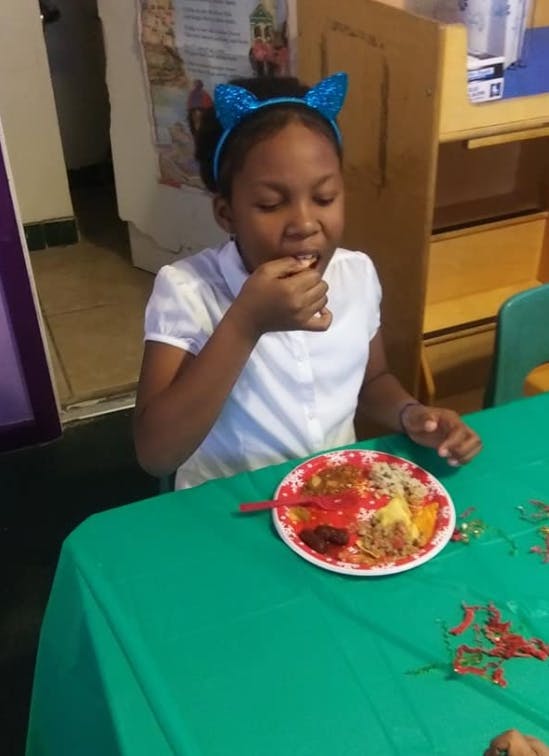 Child eating from a plate of food at a table