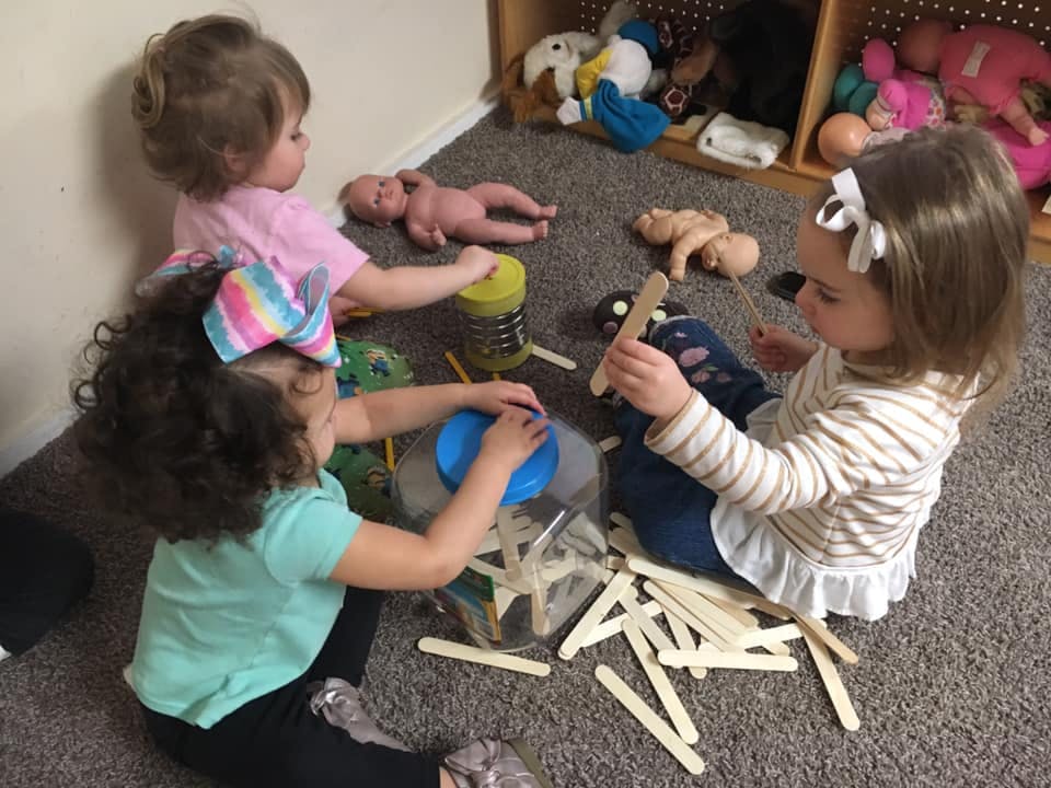 Three children playing with craft sticks on a carpeted floor
