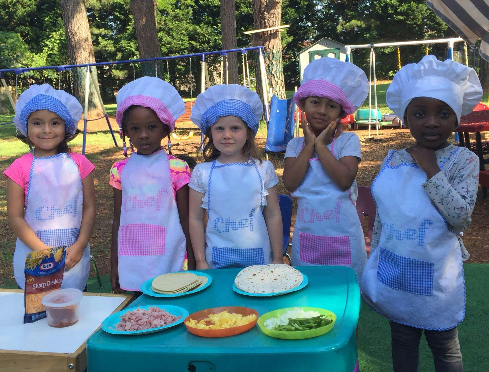 Children in chef hats and aprons standing around a table with food items for making food