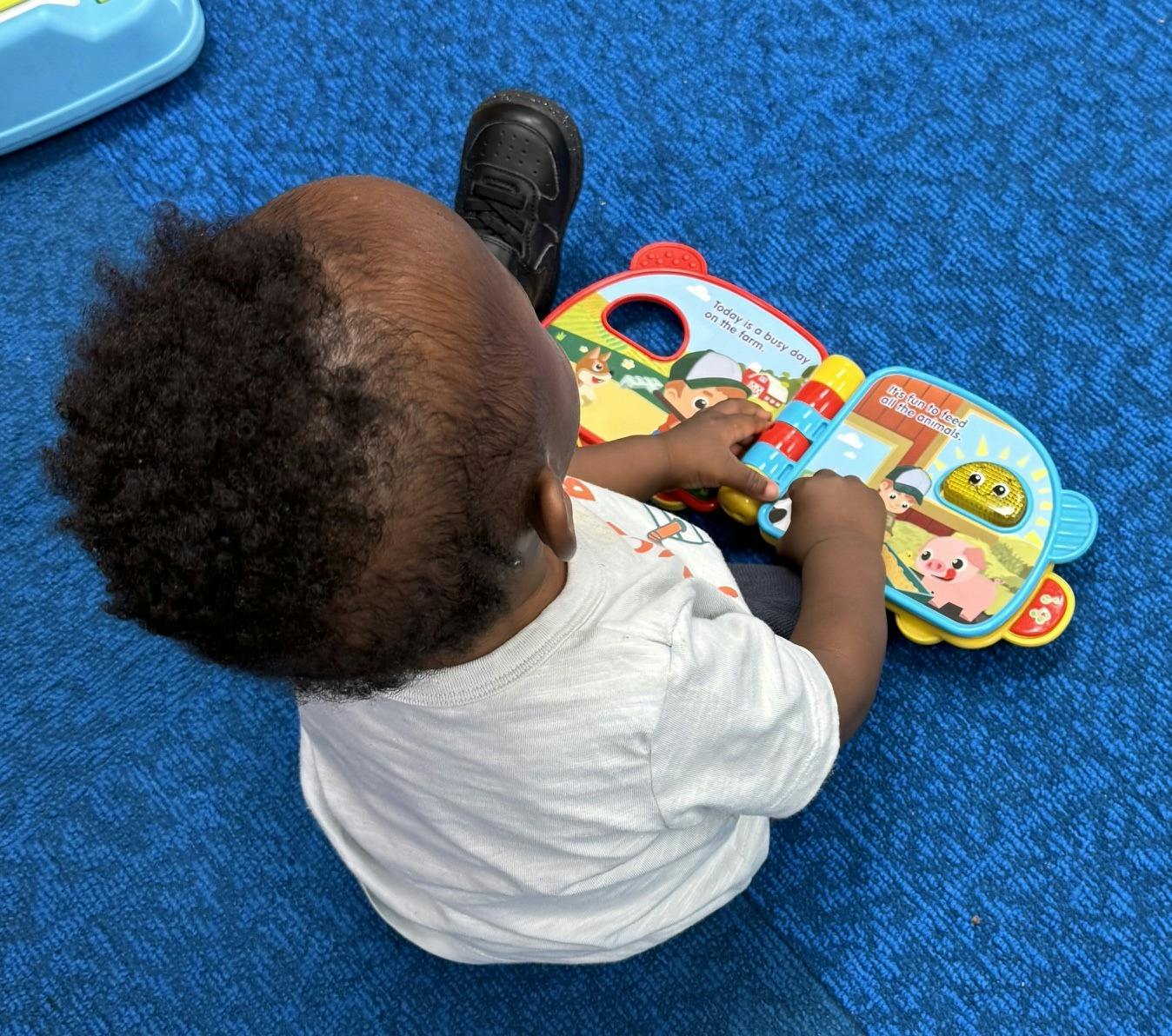 Child sitting on blue carpet playing with an interactive farm-themed toy