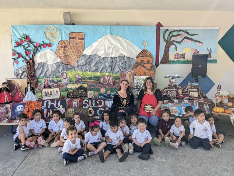 Two women with a group of children sitting in front of a decorated wall