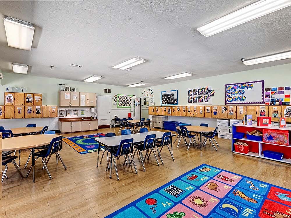 Empty classroom with small tables and chairs, colorful rugs, and decorations on walls