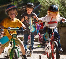 Three children riding bikes and a scooter