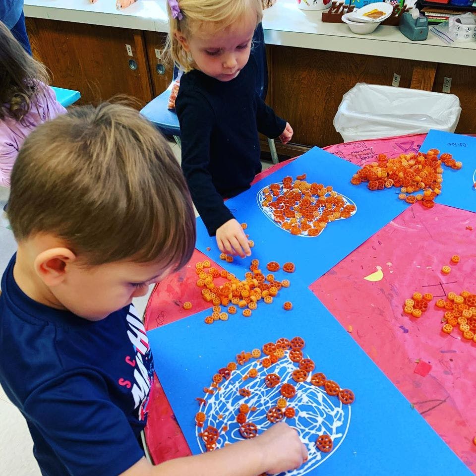 Two children doing an art project with small orange objects on blue paper