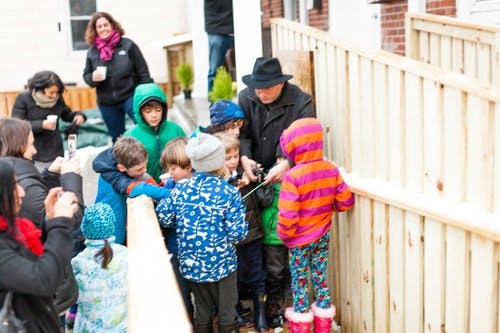 Adults and children gathered around a wooden fence