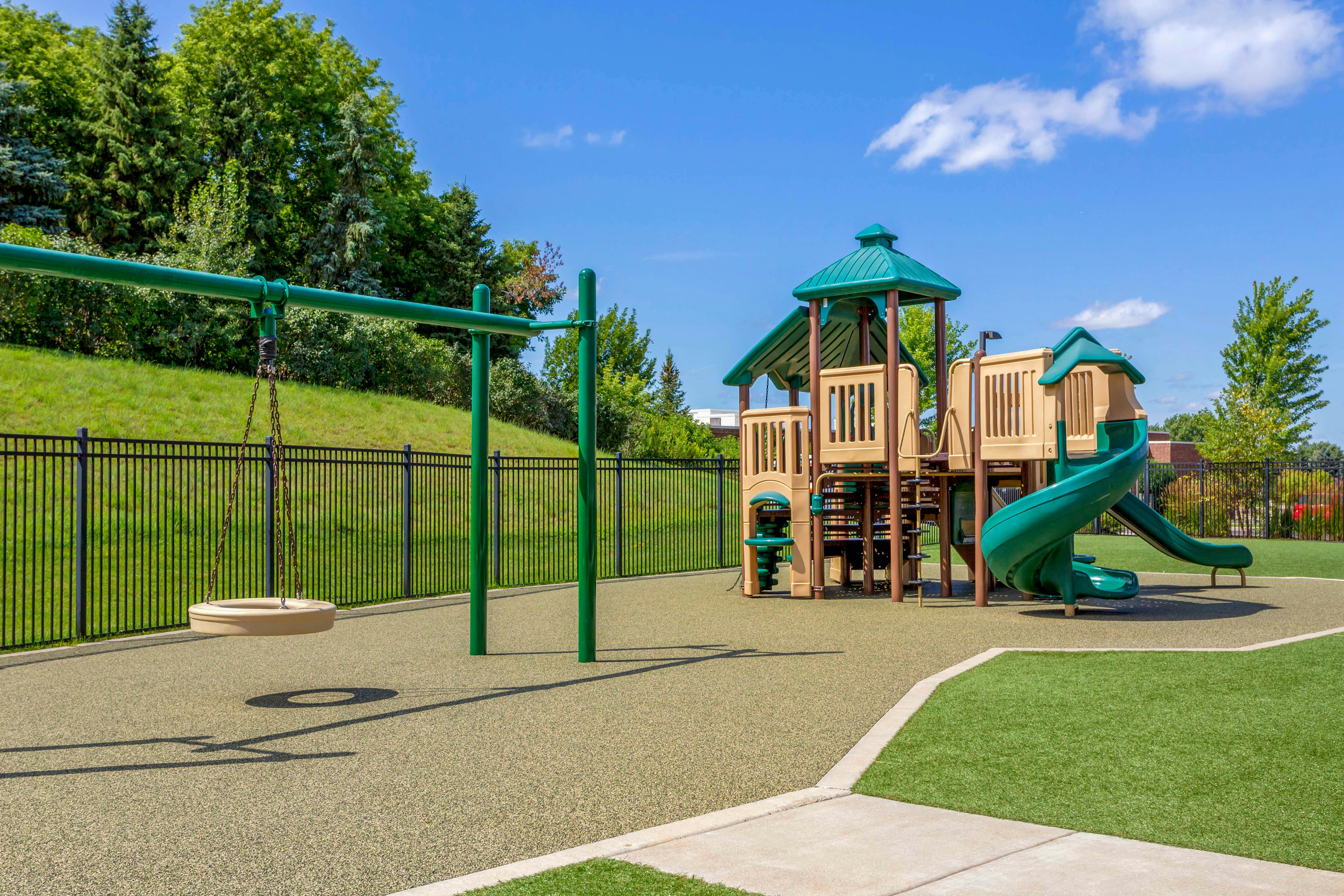 Empty outdoor playground with a green and tan playset, spiral slide, and tire swing