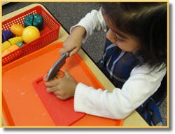 Child cutting toy fruit with a toy knife on a cutting board