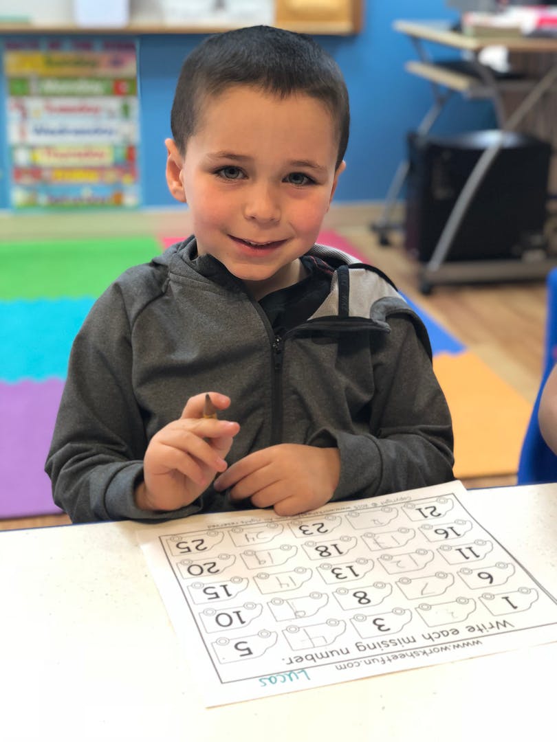 Child sitting at a table with a worksheet, holding a pencil