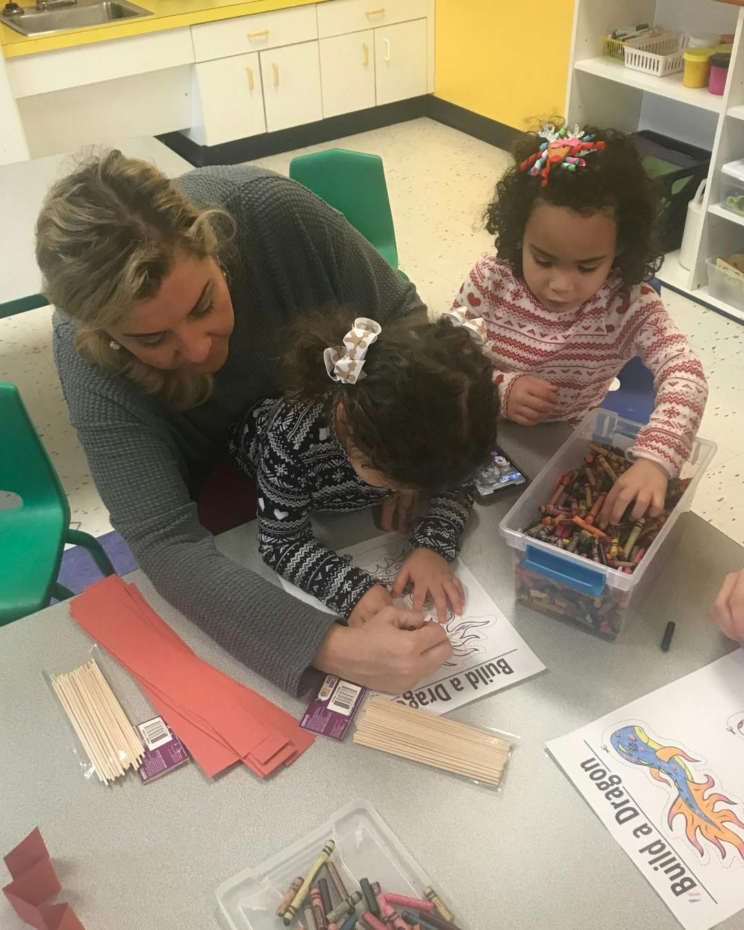 Person and two children drawing at a table in a classroom