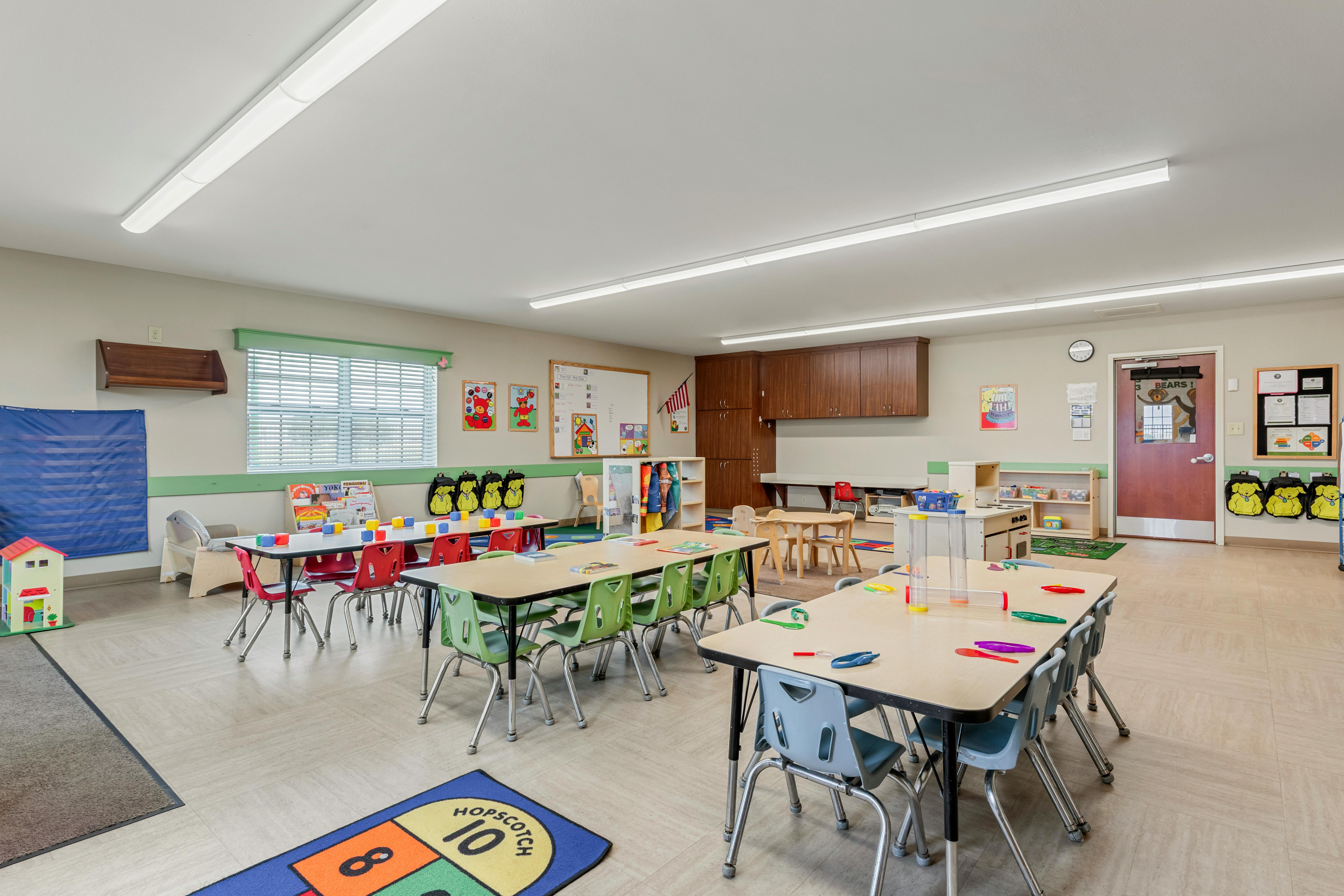 A classroom with several tables and chairs for children, a door with a \"BEARS!\" sign