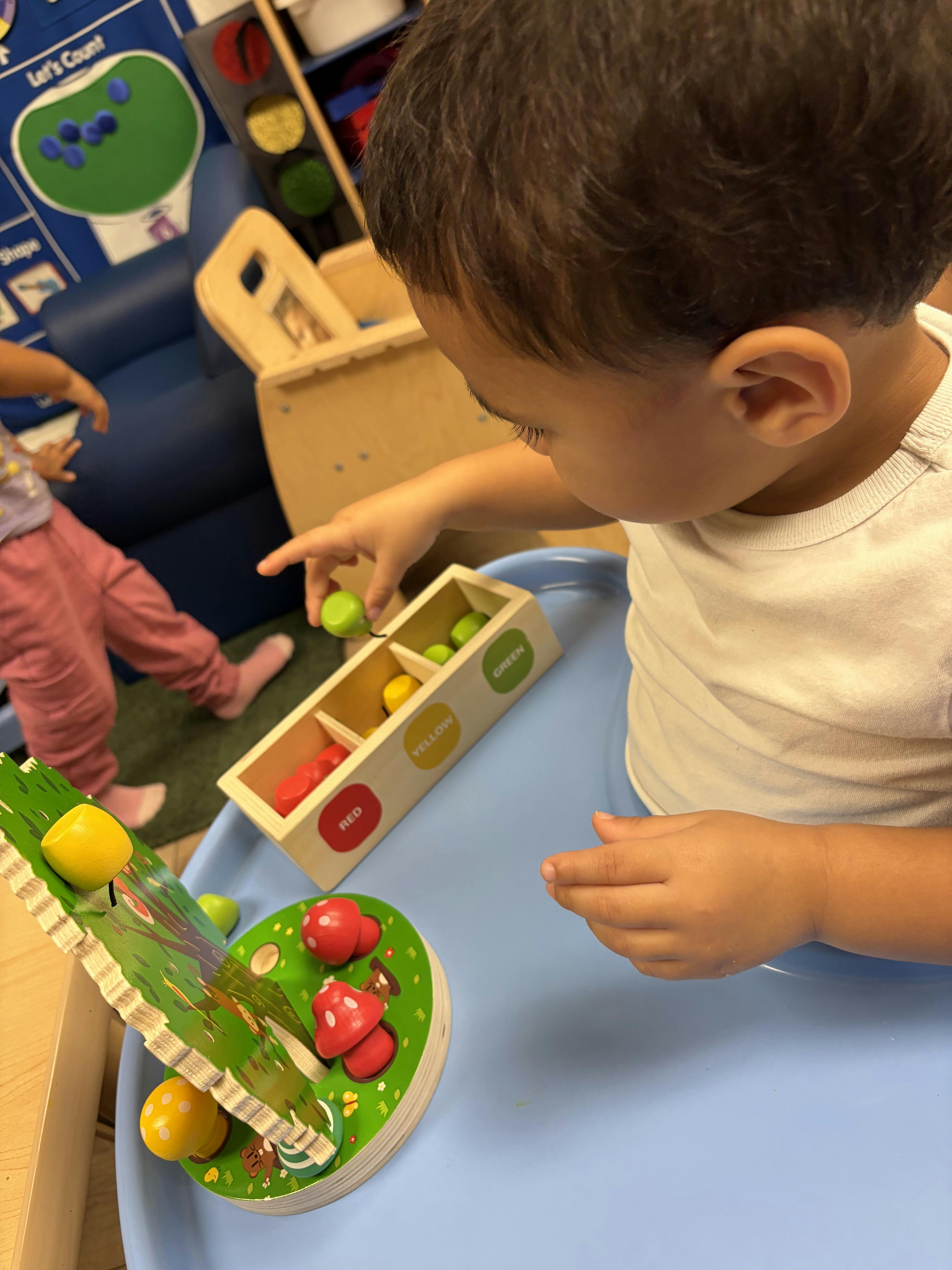Child playing with a wooden color sorting toy in a classroom