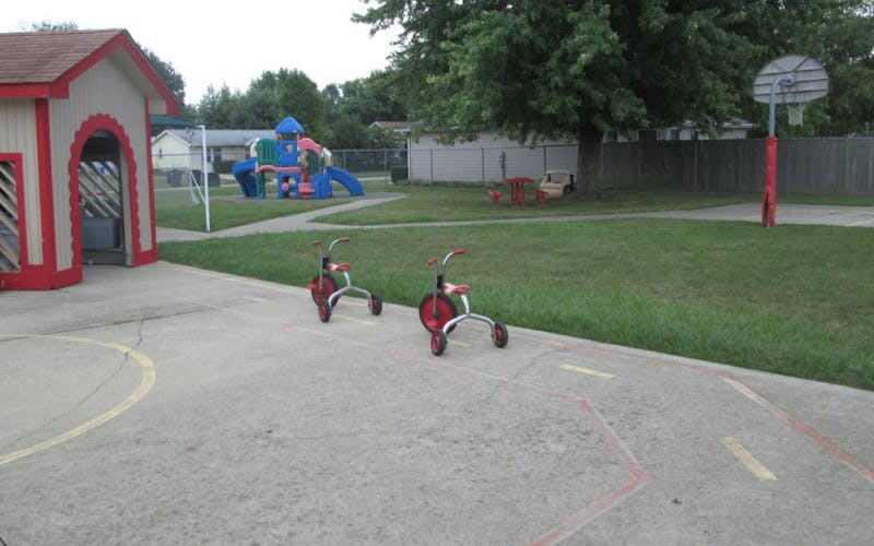 Tricycles on a paved playground with a playhouse and colorful playset