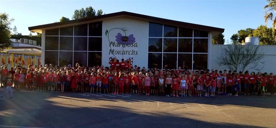 Large group of children standing in front of a building with "Mariposa Monarchs" sign