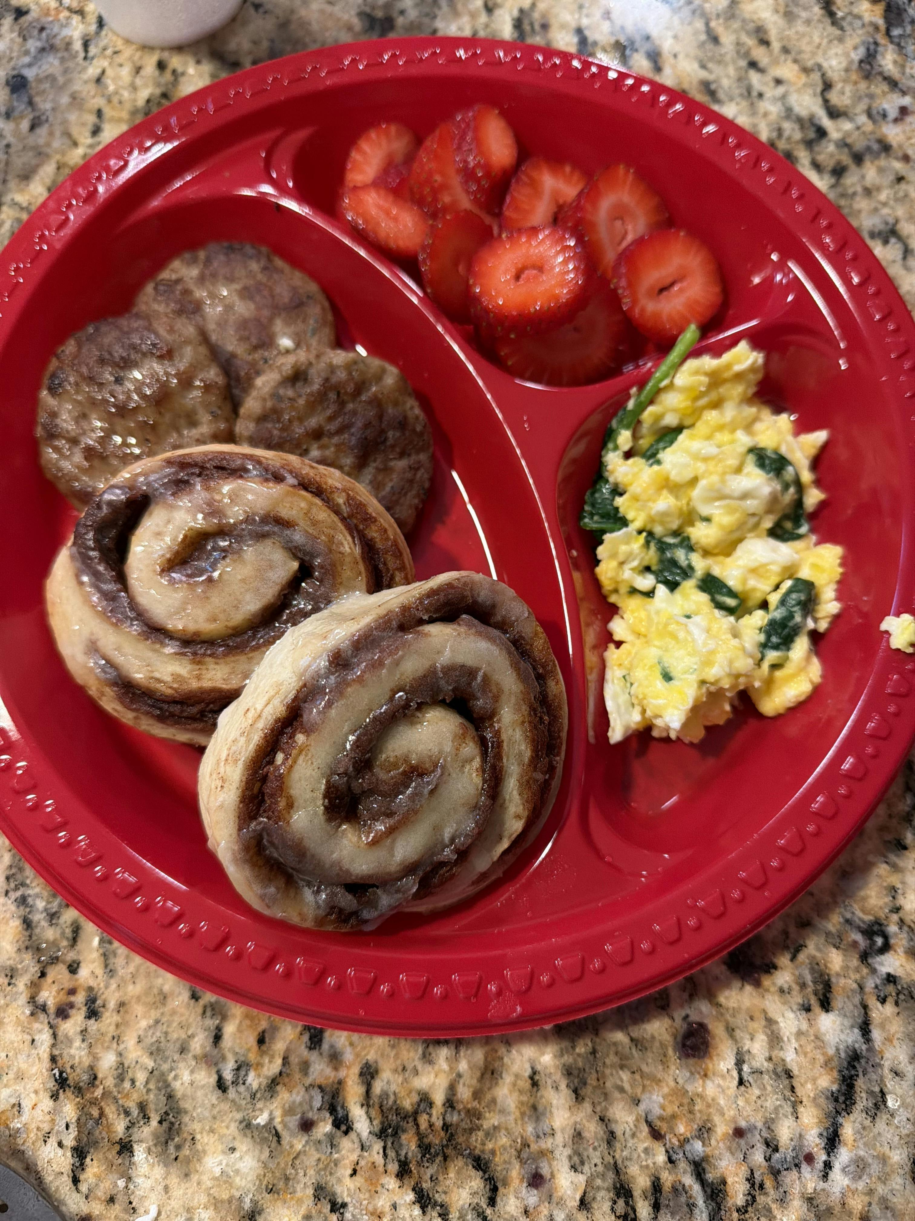 Cinnamon rolls, sausage patties, sliced strawberries, and spinach scrambled eggs