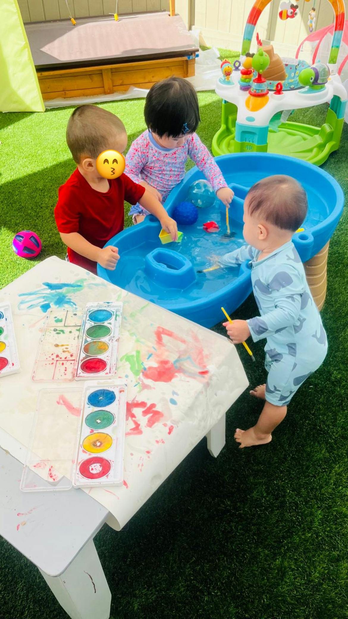 Three children playing with a water table and painting at a table with watercolors