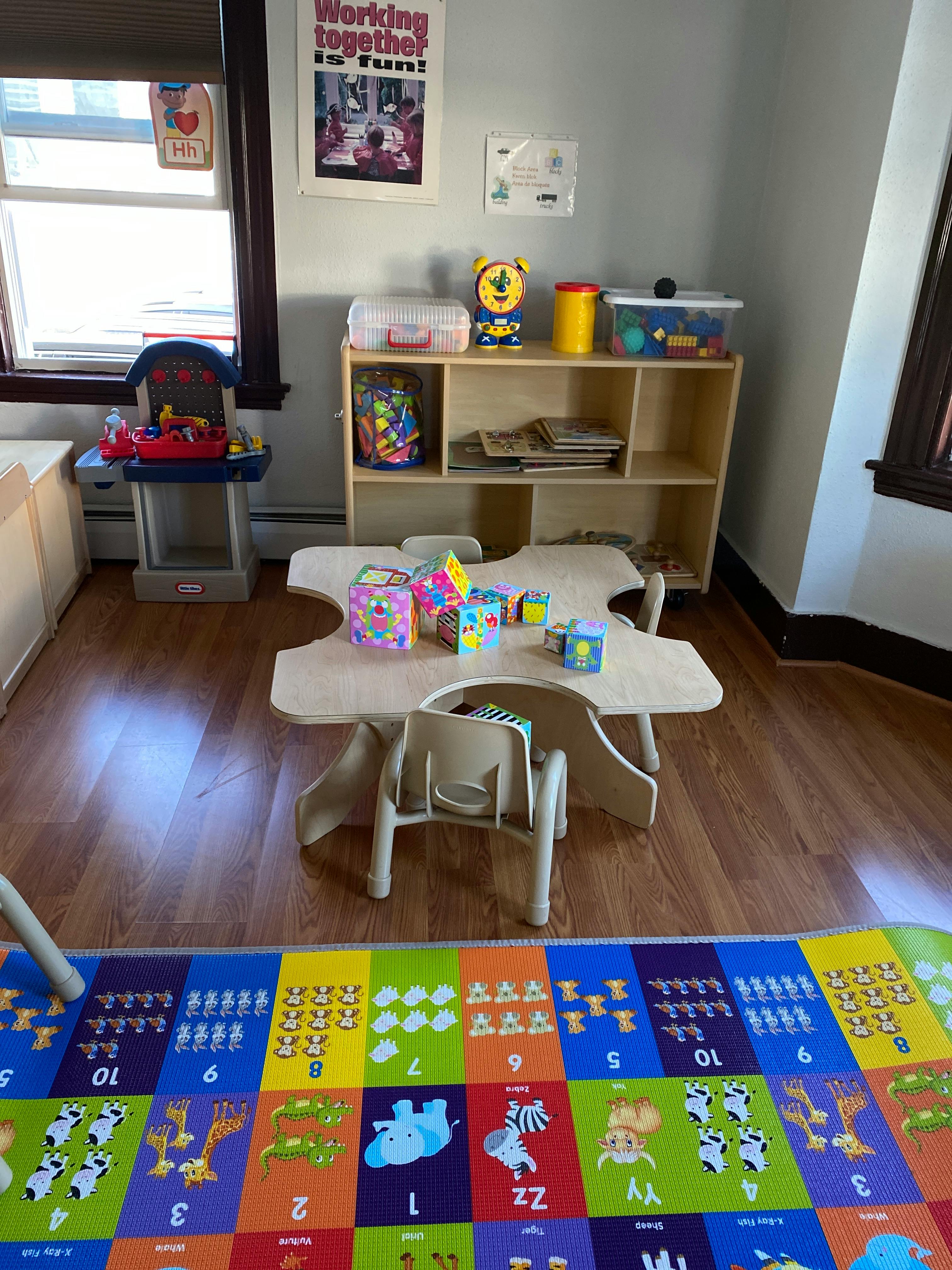 Child's classroom with small table and chairs, shelving unit, and play mat