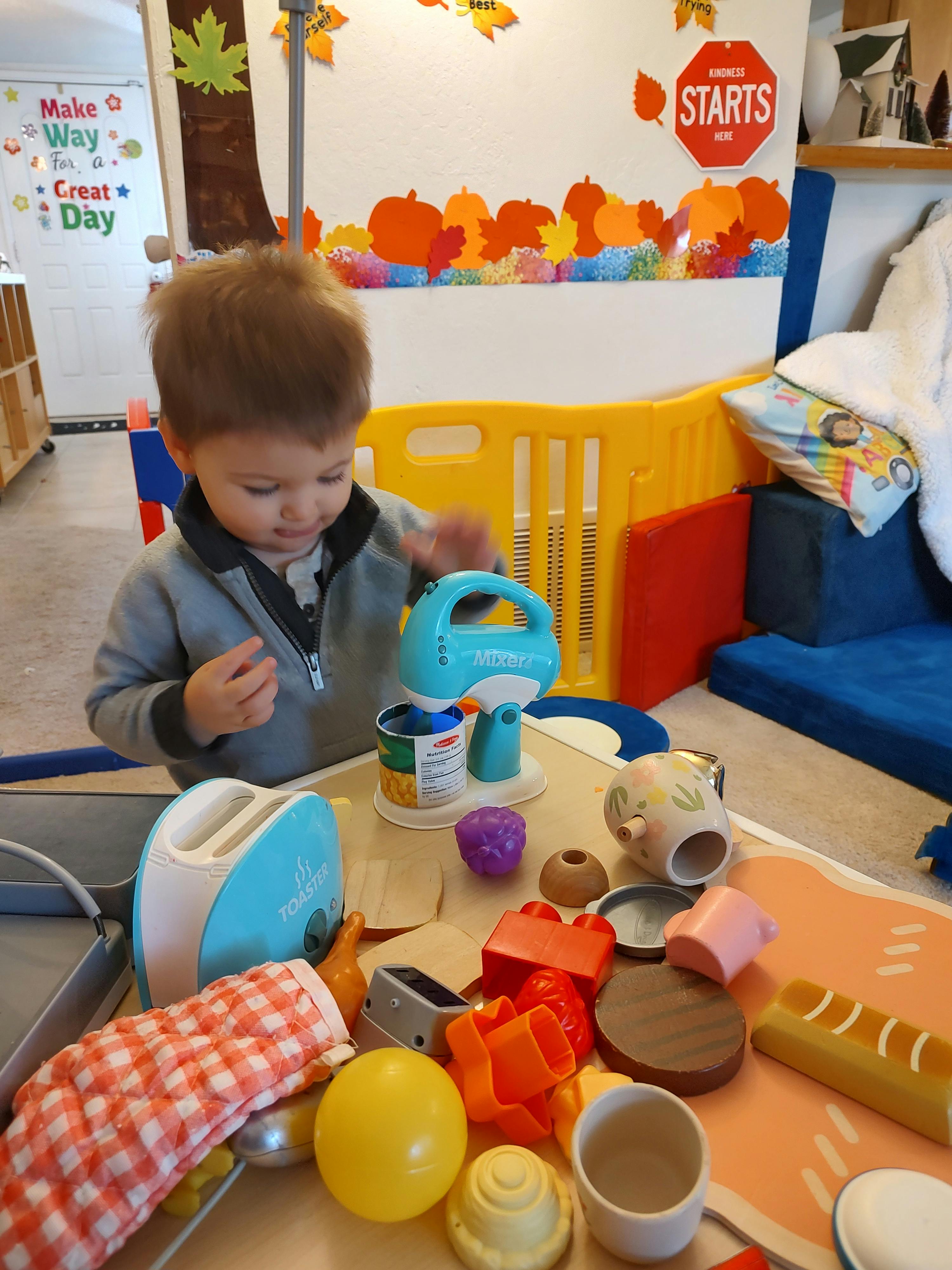 child playing with a toy mixer and other play kitchen items