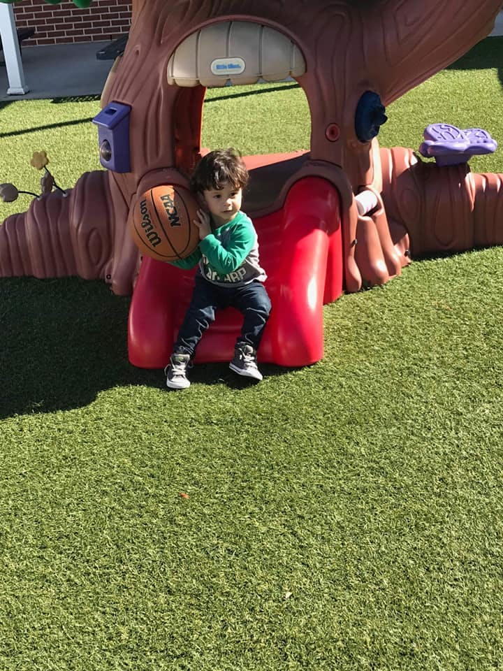 Child holding a basketball while sitting on a red play structure