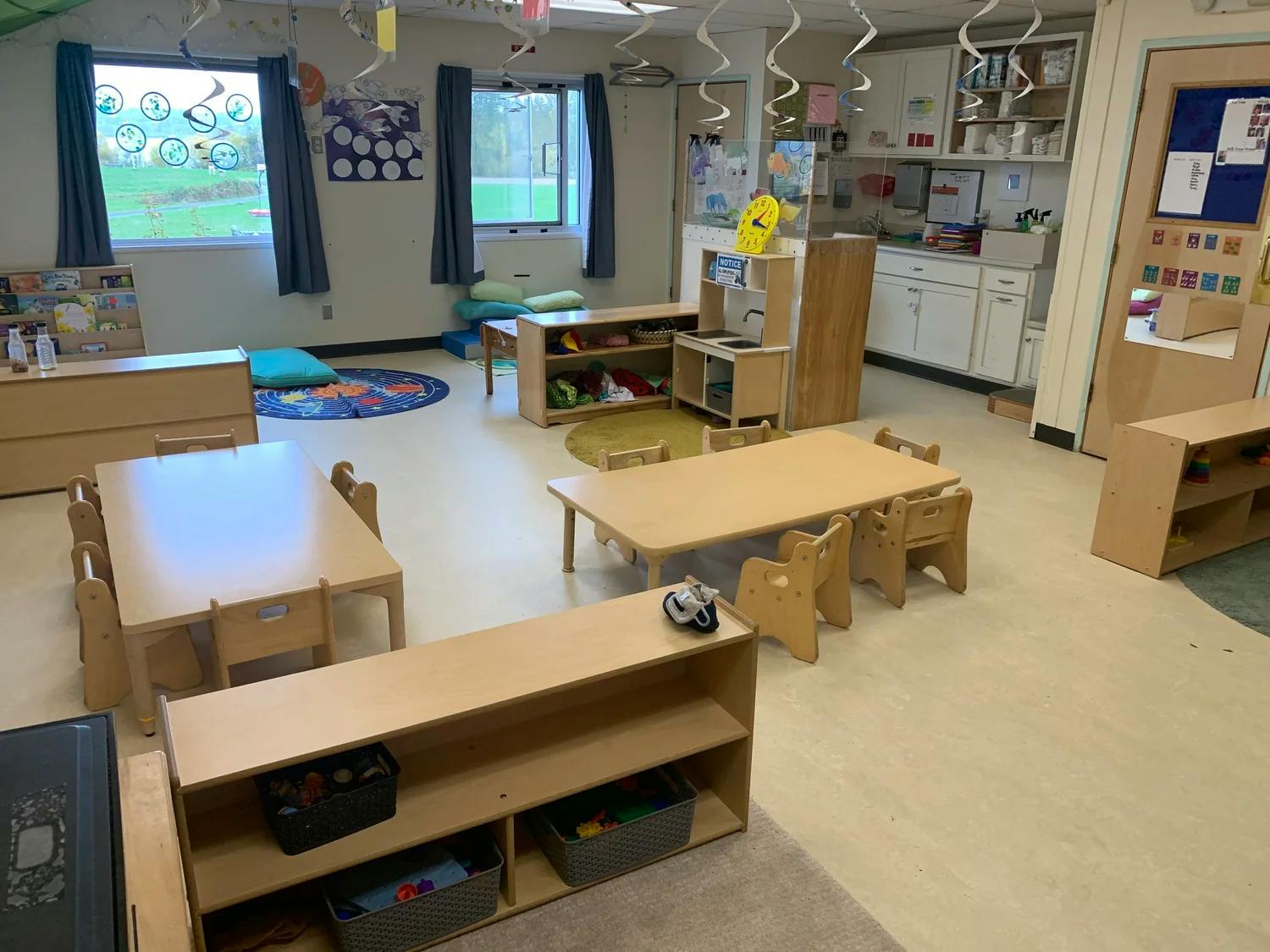 Classroom with small wooden tables, chairs, and shelves