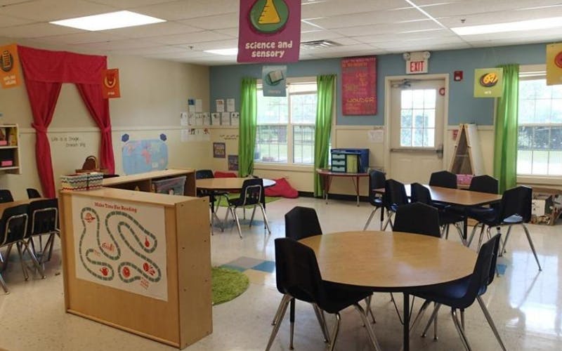 An empty classroom with small tables and chairs, bright green curtains, and colorful decor