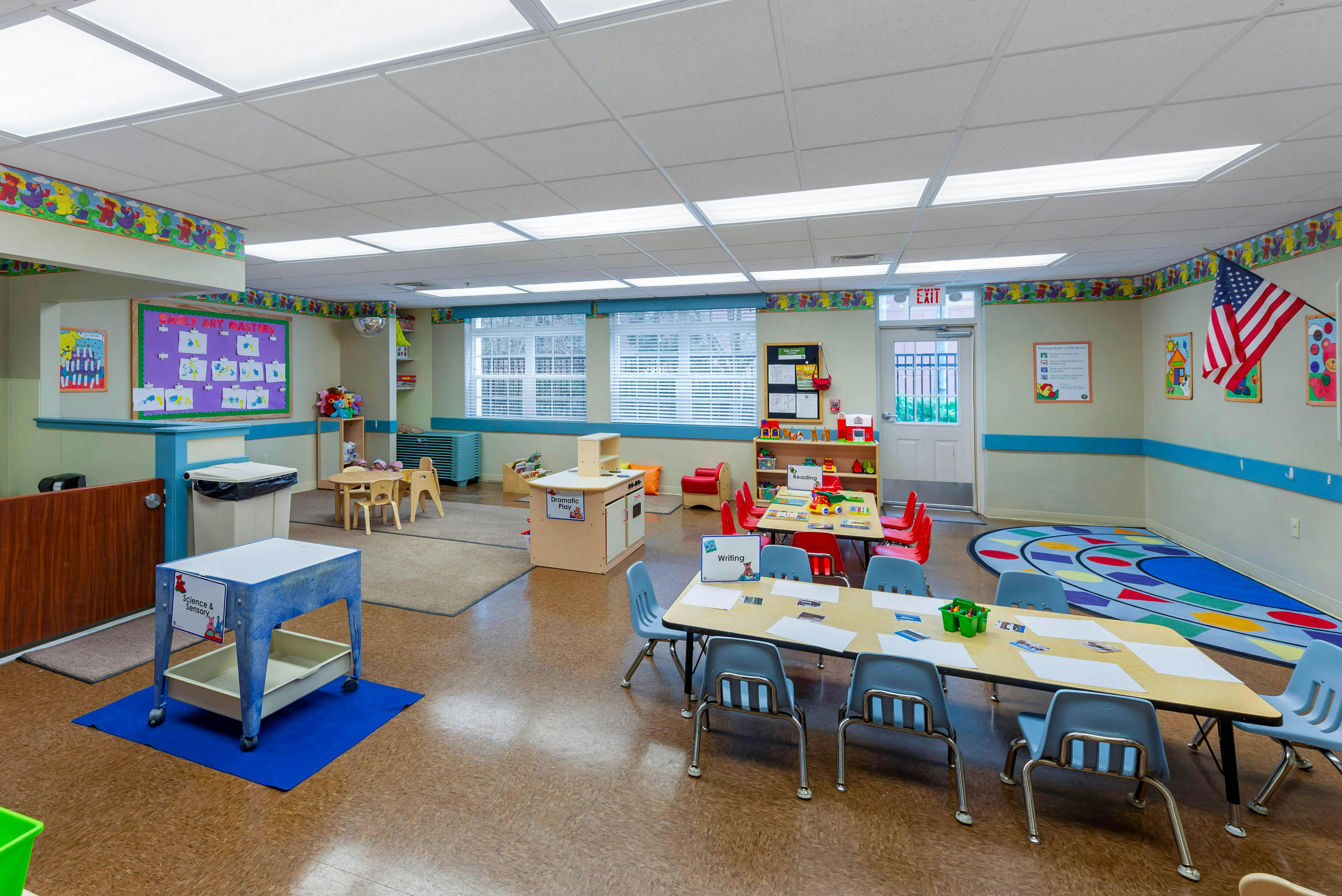 Empty classroom with small tables and chairs, play kitchen, and colorful decor