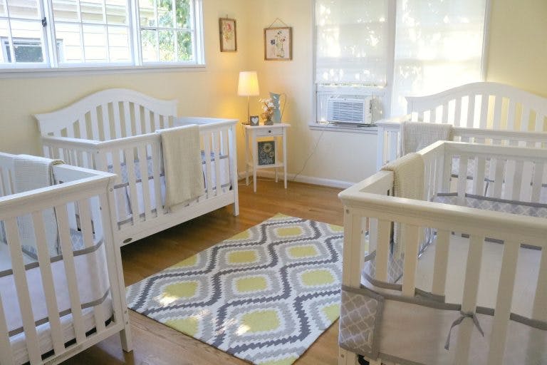 Three white cribs in a room with a patterned rug