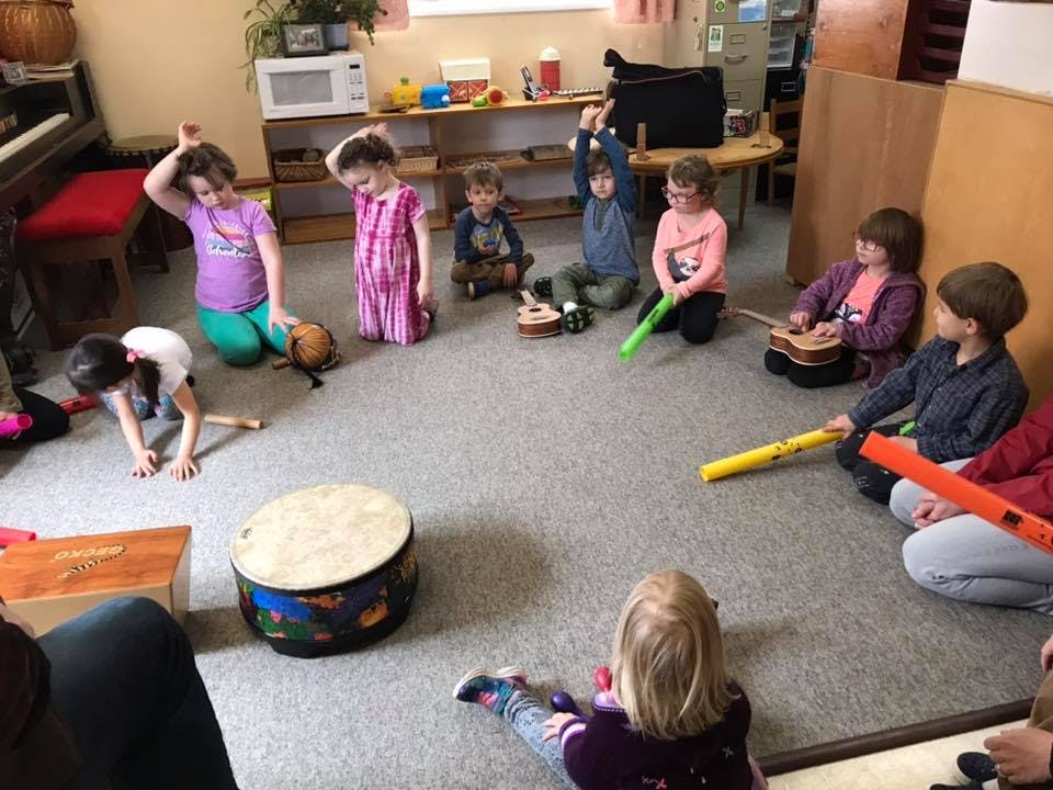 Children playing musical instruments in a circle on the floor