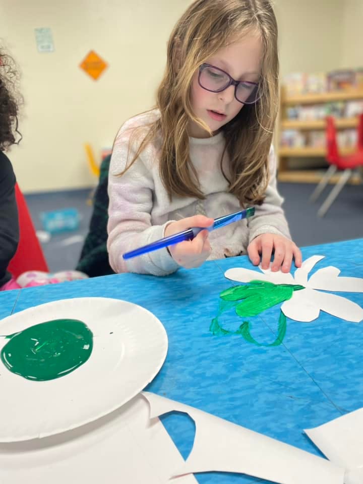 Child painting a paper flower green with a paintbrush