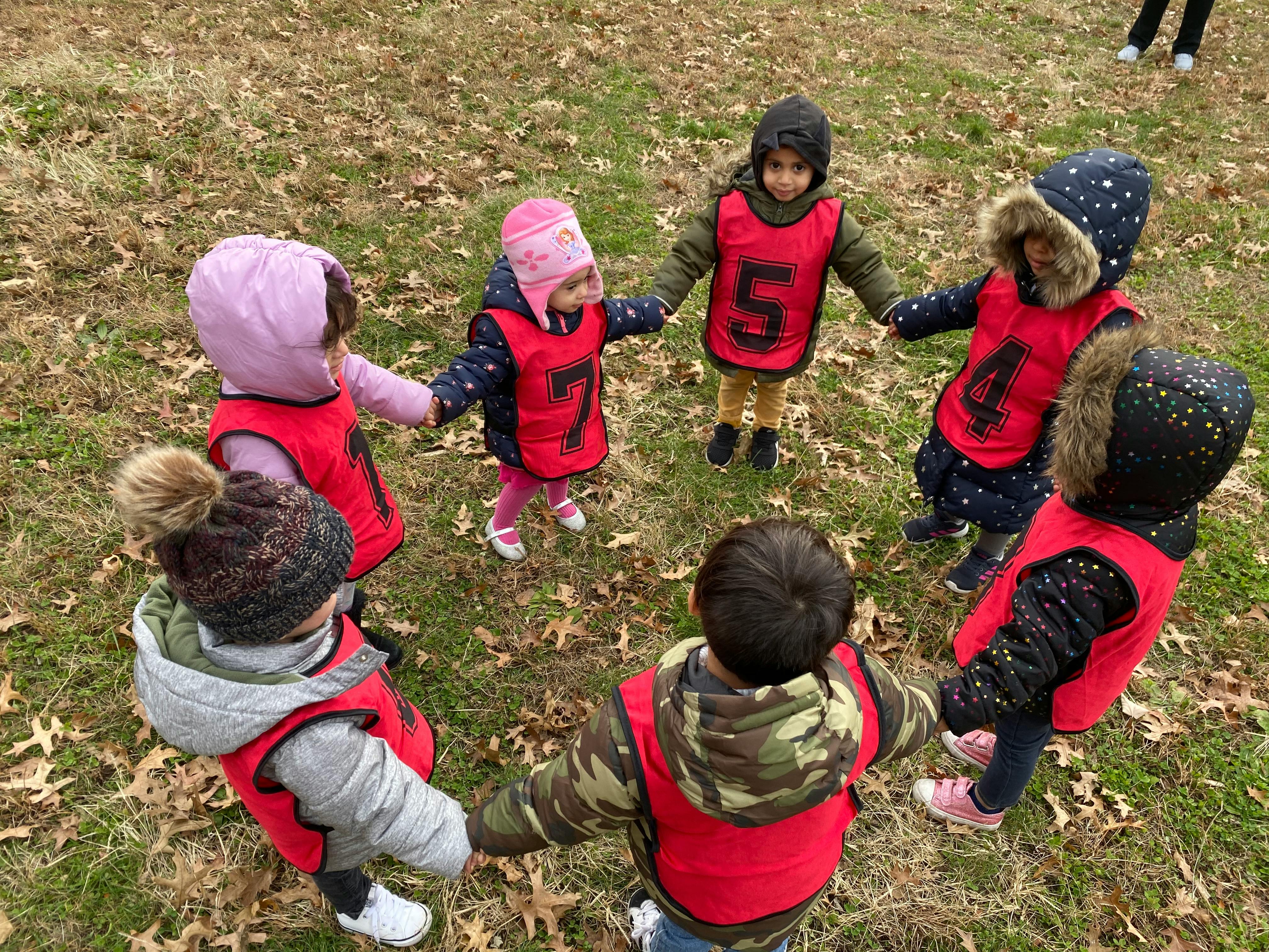 Children in red vests holding hands in a circle outdoors