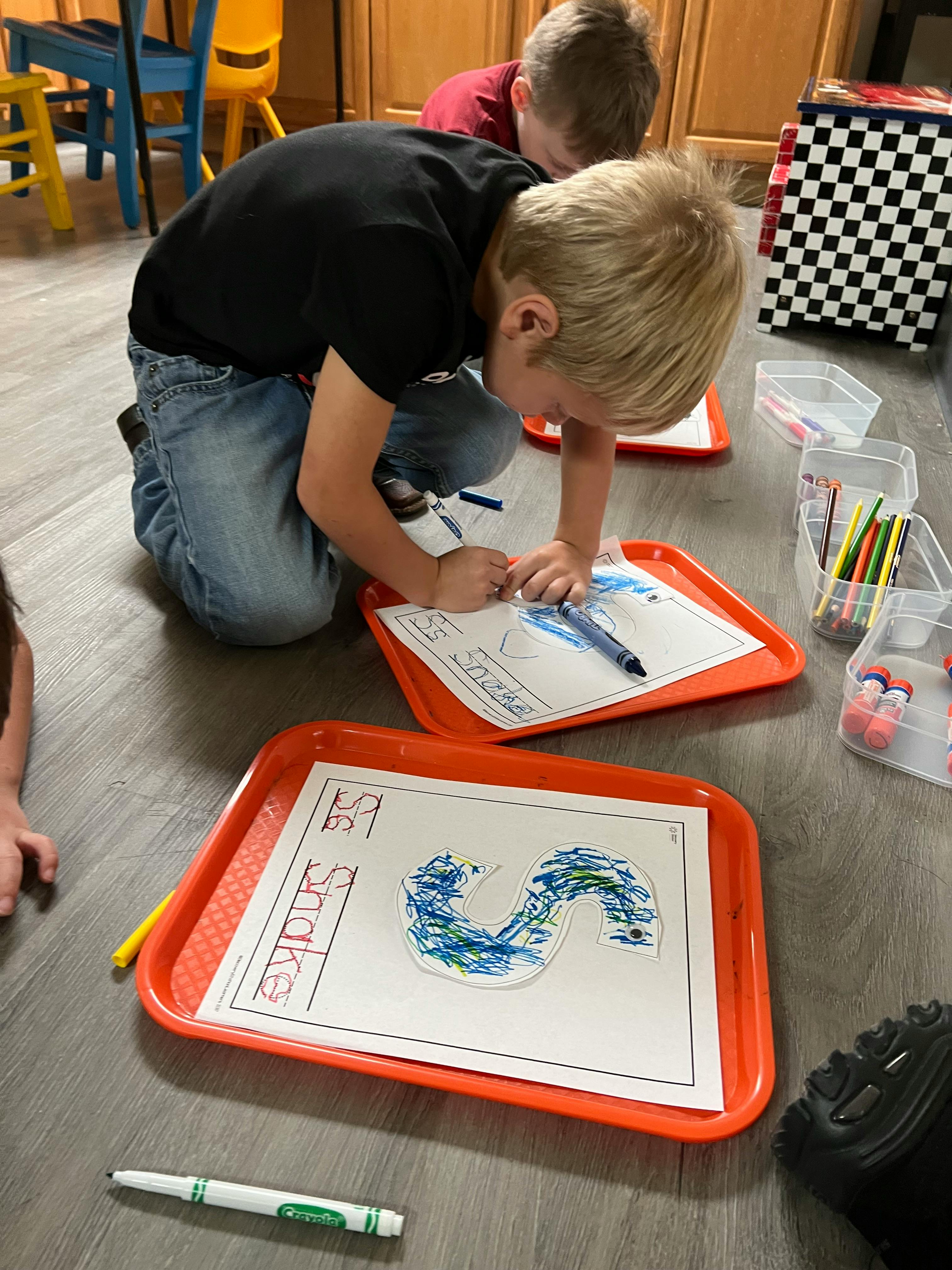 Child kneeling on floor coloring a letter S on a worksheet