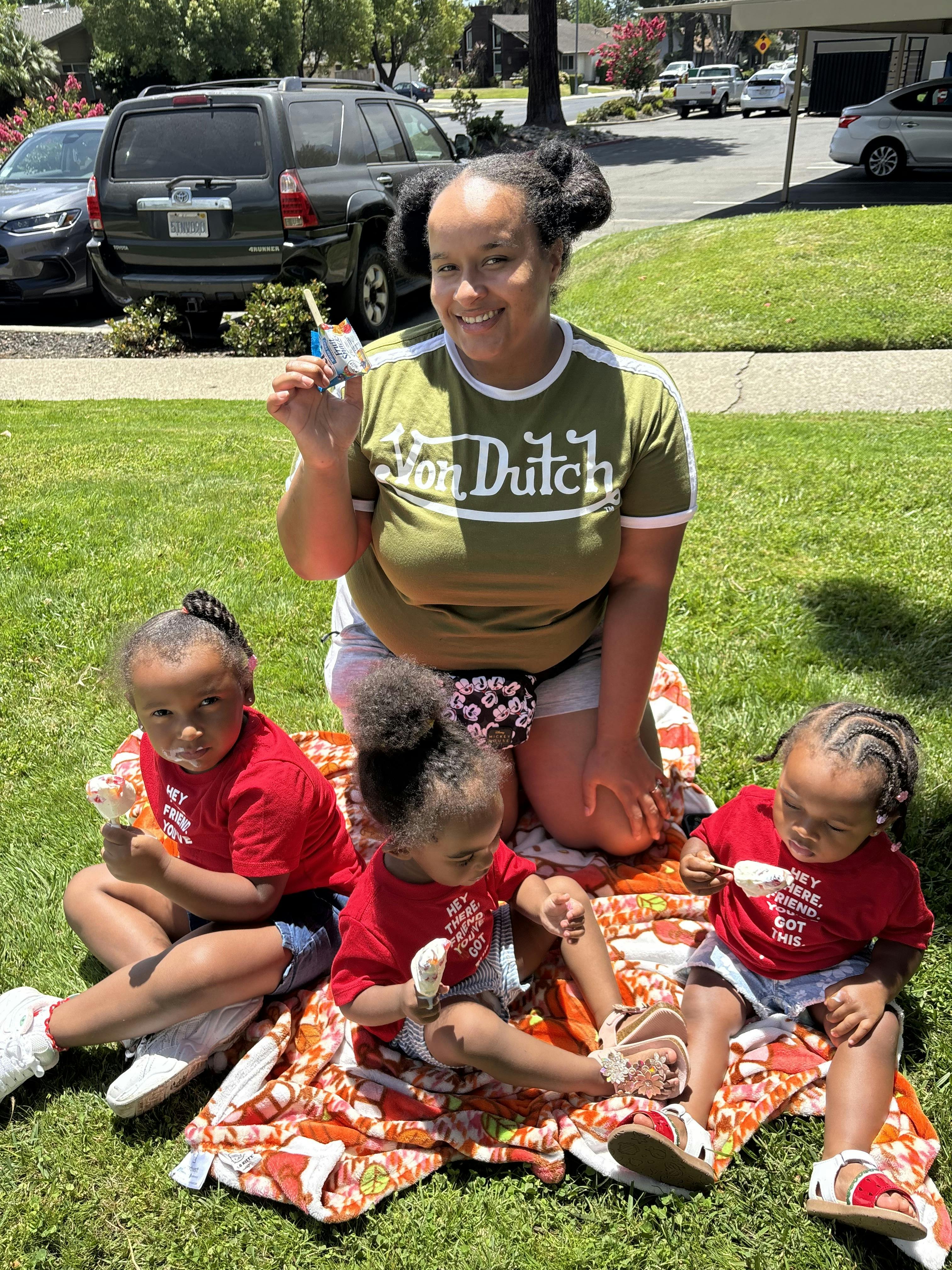 Adult and three children eating popsicles on a blanket in the grass