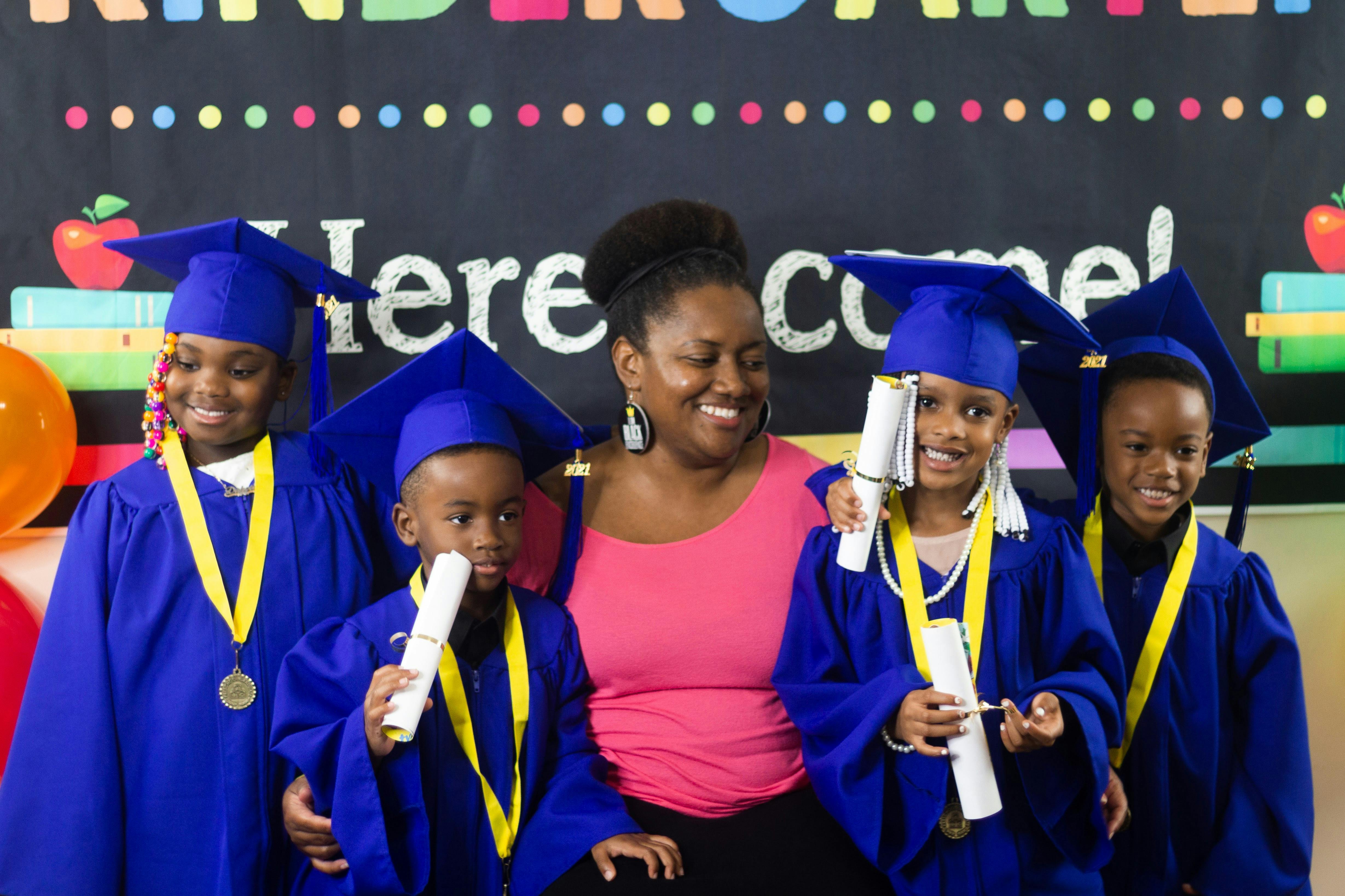 Adult and four children in graduation caps and gowns holding diplomas