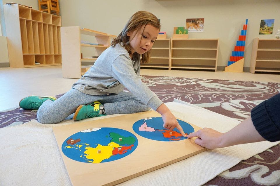 Child and person pointing at a world map puzzle
