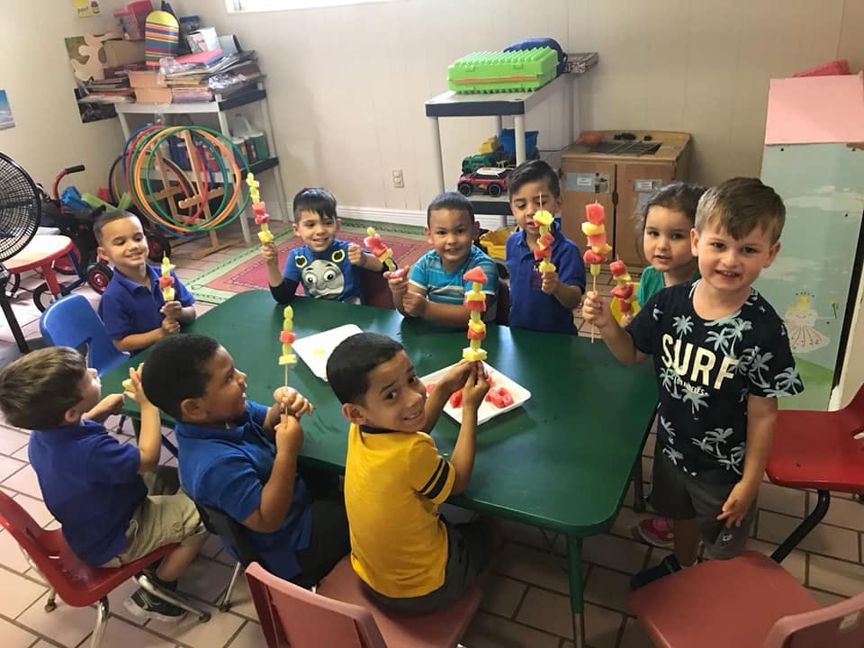 Children sitting at a table holding fruit skewers