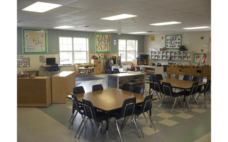 An empty classroom with multiple tables, chairs, and learning materials