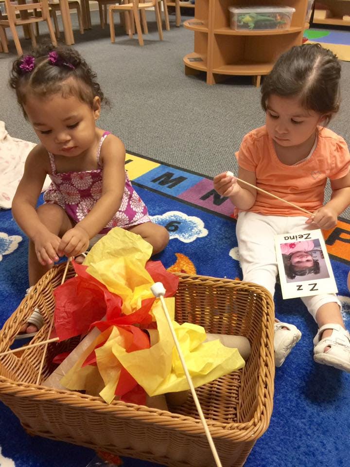 Two children playing with a basket of colorful tissue paper and sticks
