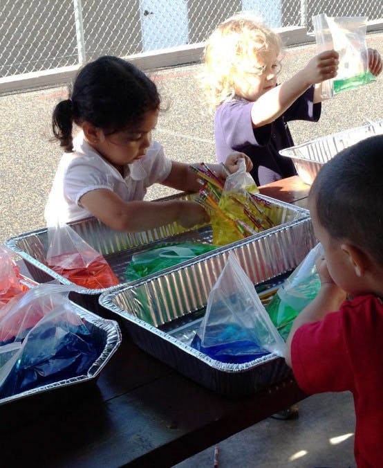Children playing with colorful liquid in plastic bags in aluminum pans