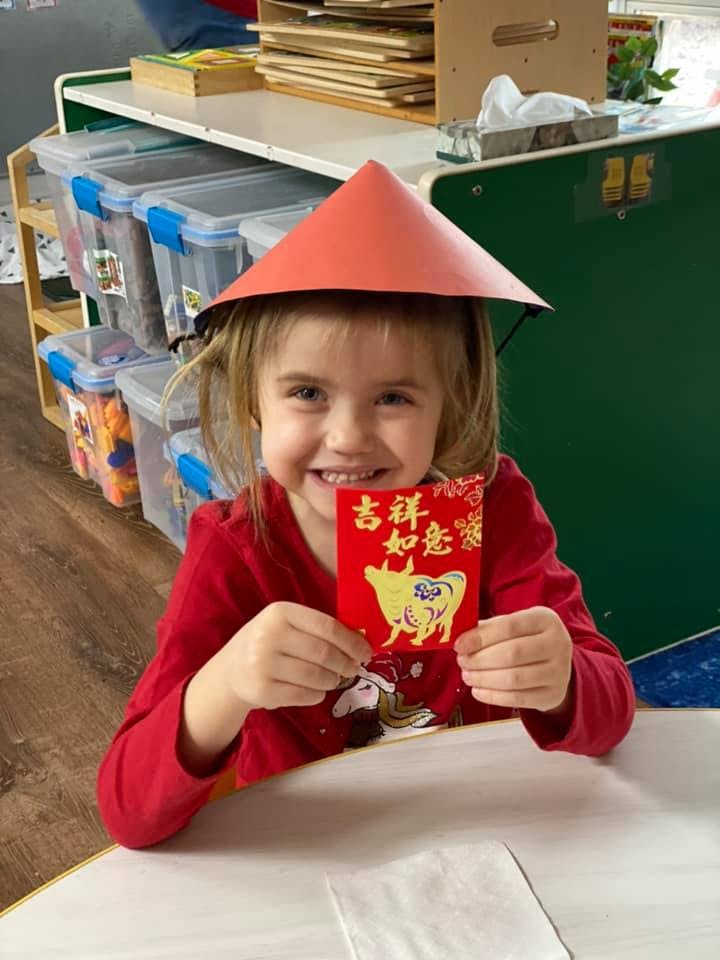 Child wearing a red conical hat and holding a red envelope with text