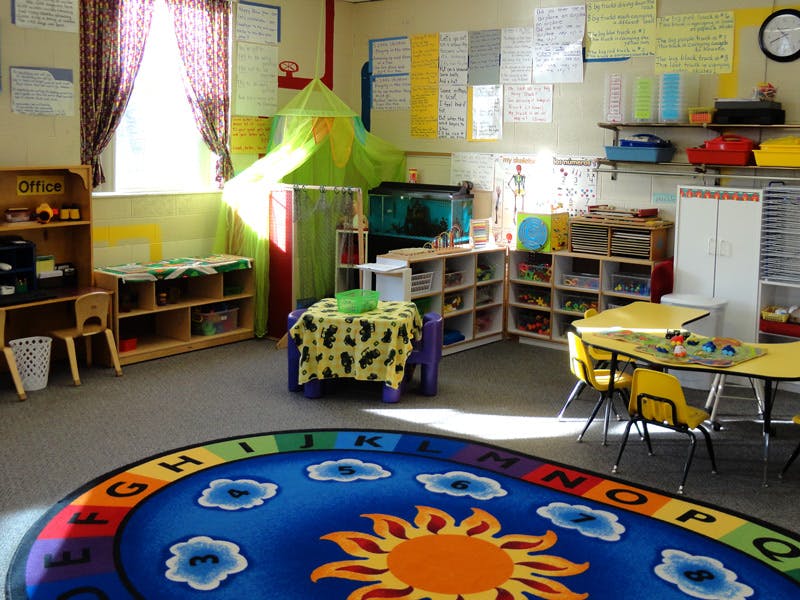 Classroom with a colorful rug, small tables, and shelves