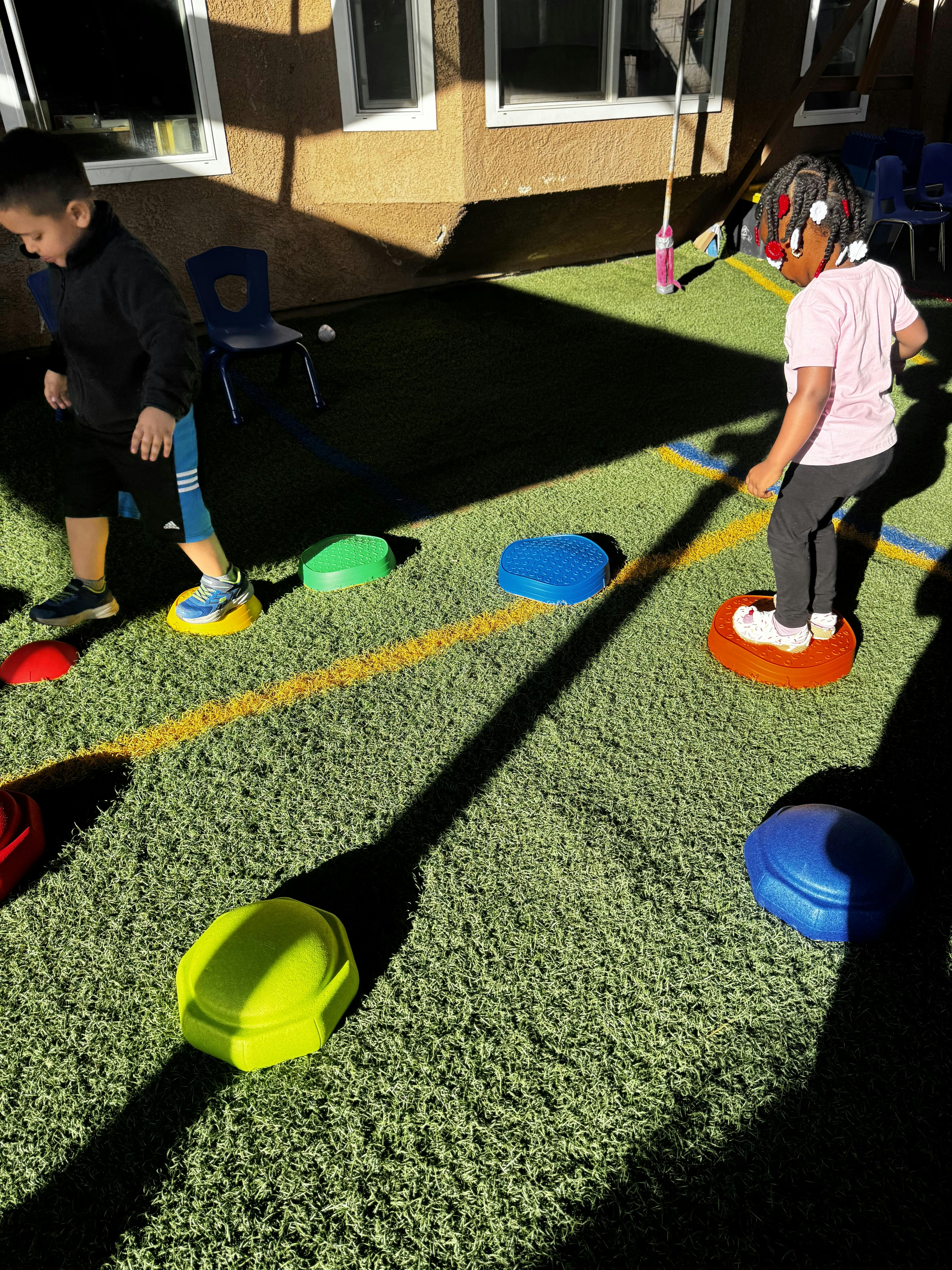 Two children playing on colorful stepping stones on artificial grass