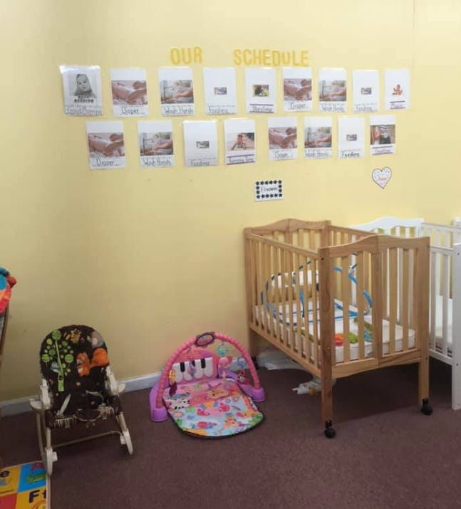 Nursery room with cribs, baby play mat, high chair, and schedule on wall