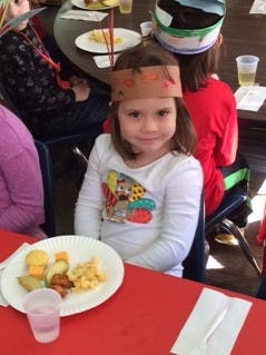 Child wearing a paper crown sitting at a table with a plate of food