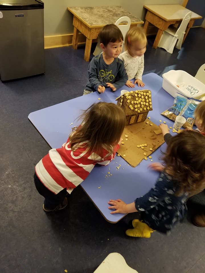 Children decorating a gingerbread house at a table