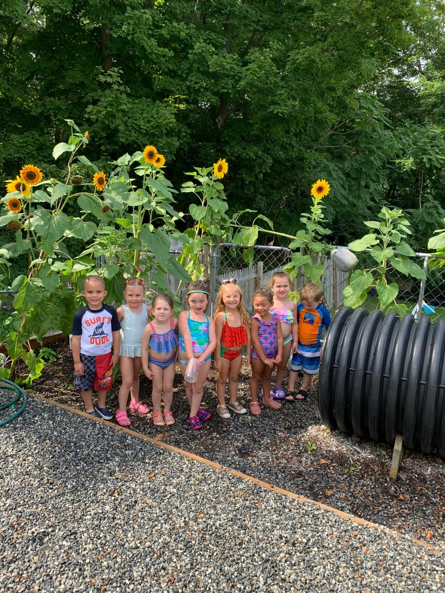 Group of children in swimsuits standing in a garden with sunflowers
