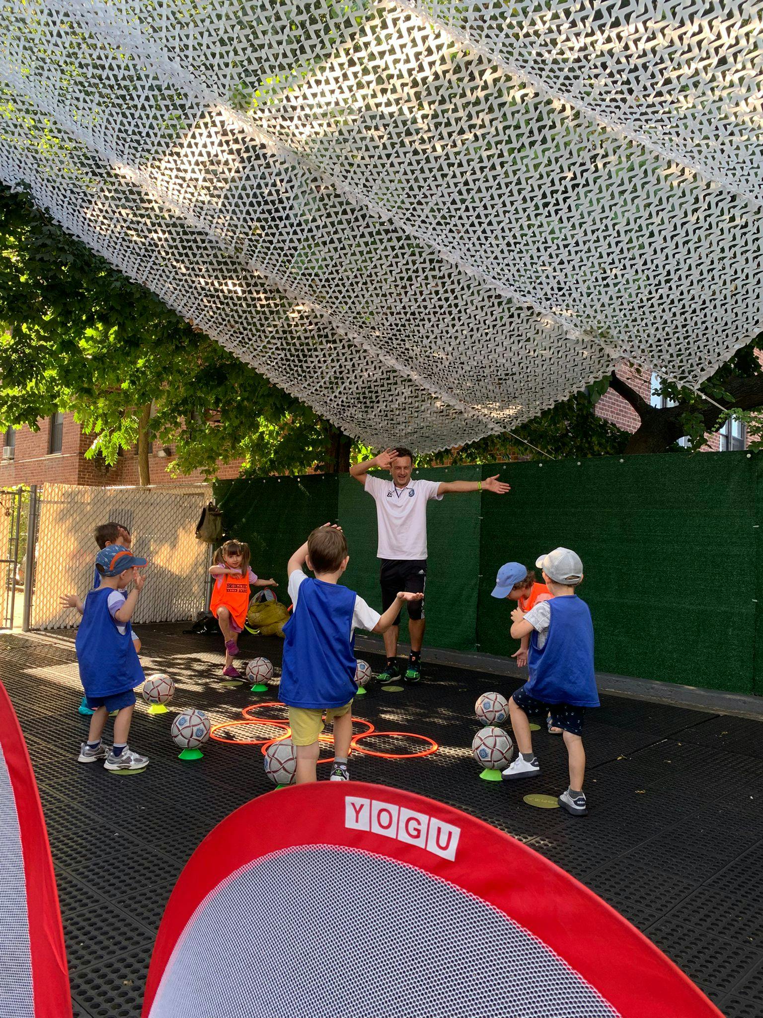 Adult with arms out supervising children playing with soccer balls